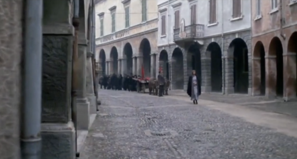 still image from the film "1900": through the main street of town a solemn march of peasants, with the bodies of their dead children murdered by fascists on display to the closed windows and doors of the town.