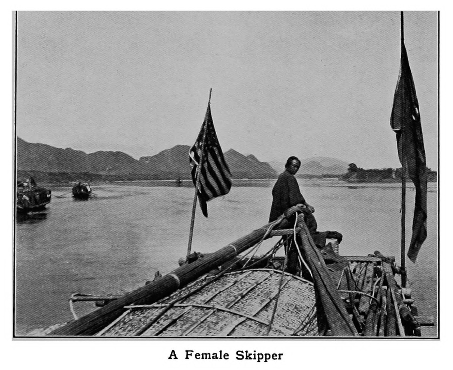 black and white photograph titled "A Female Skipper" - a woman at the head of a boat that has a Chinese and US flag.