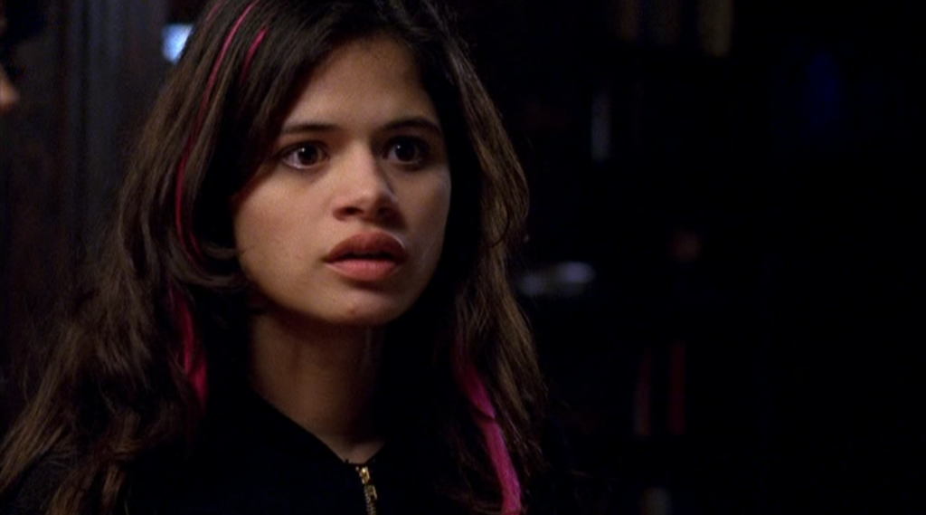 Melonie Diaz as Anna: looking serious, dark hair with pink streaks.