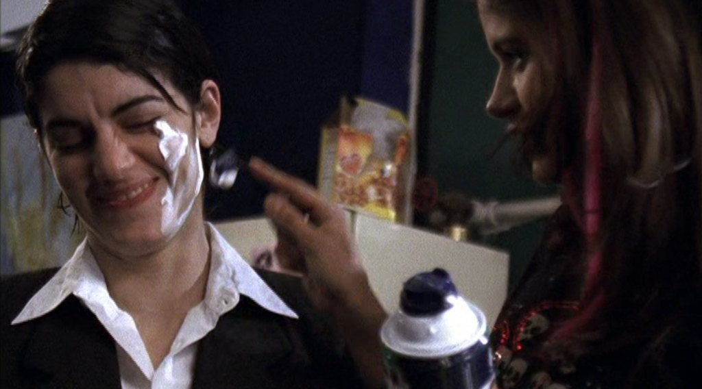 Aggie in a suit laughing with shaving cream on his cheek, while Anna shaves him.
