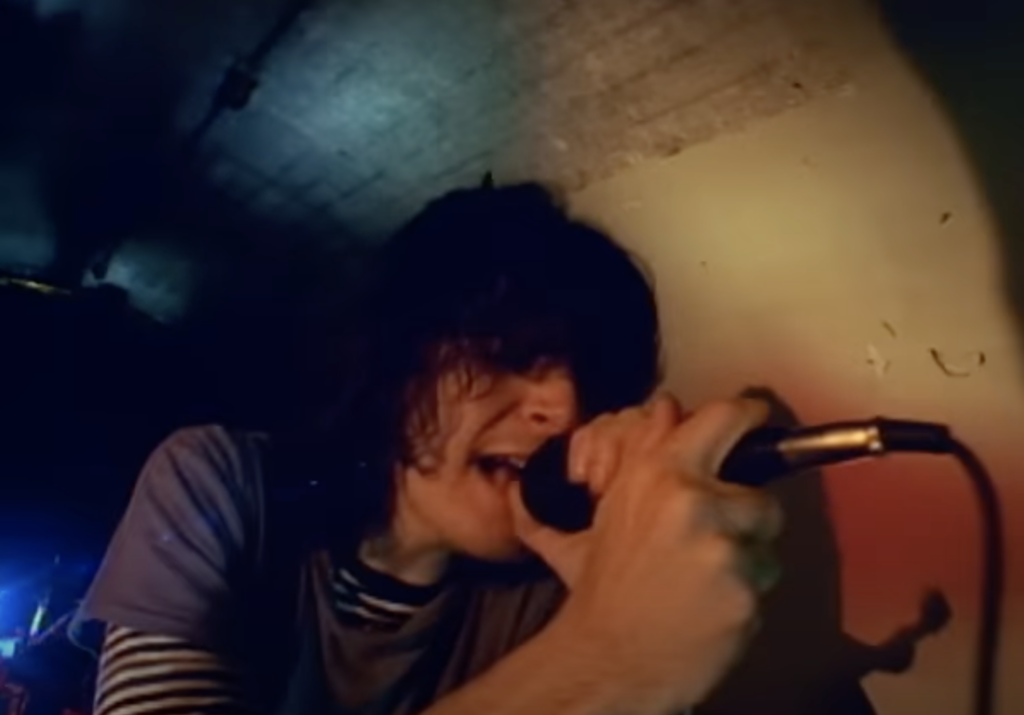 still from "Under My Skin" music video of Kevin singing into a microphone in a tunnel